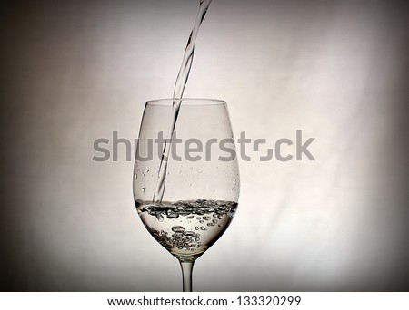 water pouring into wine glass black with off white or grey background