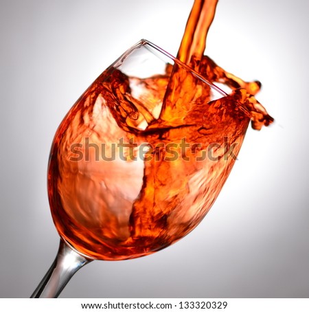Tilted wine glass filled up with red liquid until splash with grey or off-white background