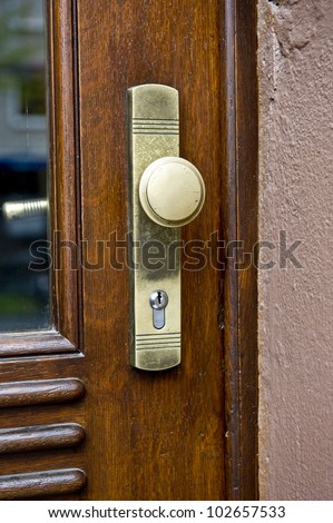 A brightly lit closeup of a golden door lock on a brown wooden door.