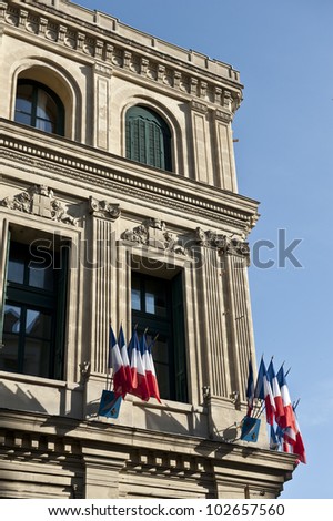 French flags posted on a ledge of the corner of a sandy brown building.
