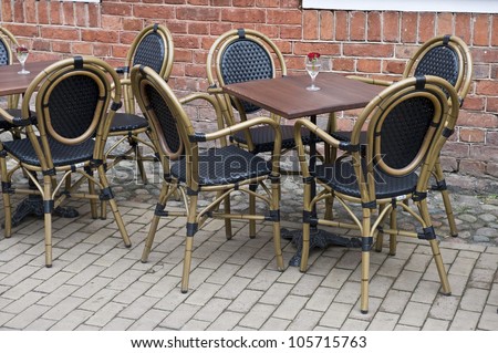 Empty square tables and chairs with rose centerpieces in wine glasses on a patio outside of a restaurant.
