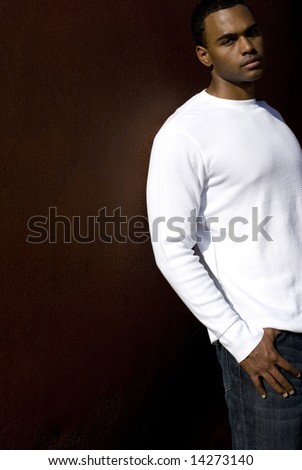 Attractive young African American male playing posing in a white t-shirt and jeans against a solid brown wall.