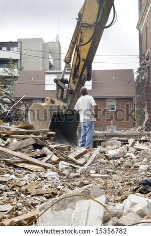 A construction worker inspects the scoop on a power shovel, amid the debris field of a partially-demolished building.