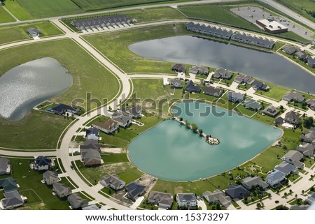 The curving streets of a suburban housing development surround a small blue pond, as seen from the air.