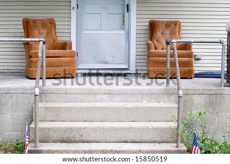 Two orange lounge chairs on the front porch of an   American home.