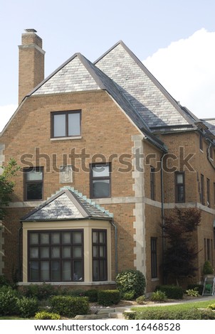 Big bay window on a beautiful brick house with a steep, sloping roof.