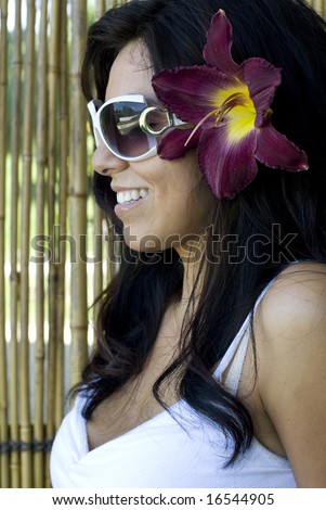 Face shot of beautiful young female smiling with flower in hair while looking down