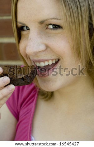 Female with pink shirt holding a brownie to her mouth