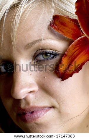 Close shot of woman with green eyes with orange flower in her hair