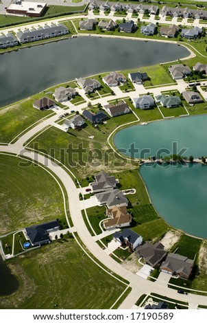 The curving streets of a suburban housing development surround a small blue pond, as seen from the air.
