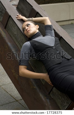 Attractive model posing with arm in air leaning against steal beam in the daytime