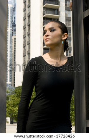 Female in black dress posing against a black wall on a sunny day