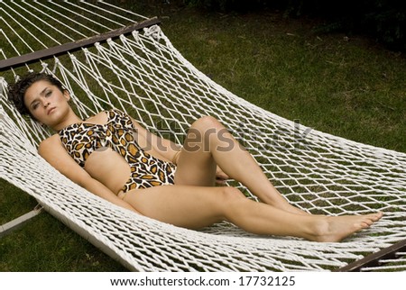 Girl in animal print bathing suit laying on her back in a white hammock on a sunny day