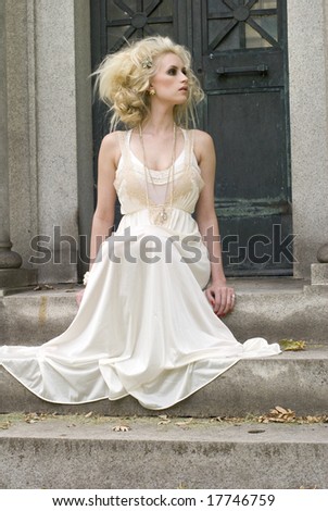 Model with big hair sitting outside in a long satin dress on a sunny day