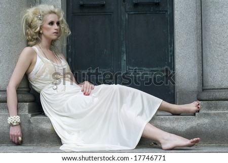 Model with no shoes leans against a gray column of an old building