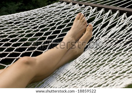 Photo of a woman\'s legs and feet lying in a white hammock on a sunny day