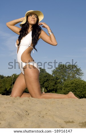 Sexy woman looks to the right while kneeling in the sand on a sunny day