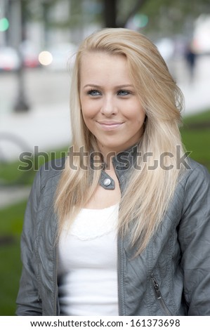 An attractive and young blond model wearing a leather jacket while posing outdoors on a cloudy day.