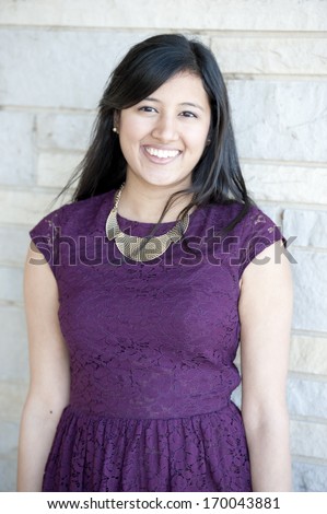 A young and happy Indian girl wearing a purple dress on a brick background on a cloudy day.