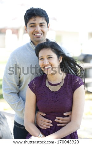 A young and happy Indian couple posing on a picnic table on a sunny day.