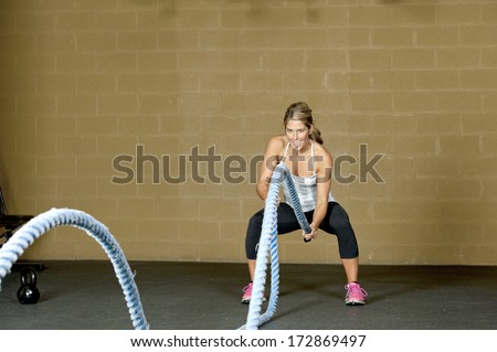 An attractive young and athletic girl using training ropes in a gym.
