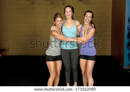 A set of three happy brunette atheltic females posing in a gym together.
