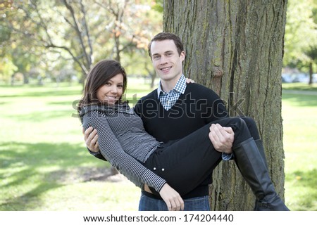 A young man carrying his wife at the park on a sunny day.