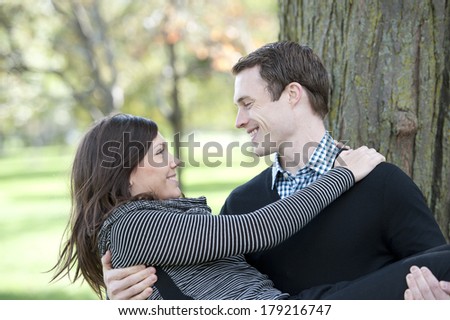 A young man carrying his wife at the park on a sunny day.