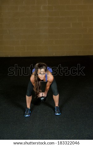 A young and athletic trainer posing with a kettlebell in a gym.
