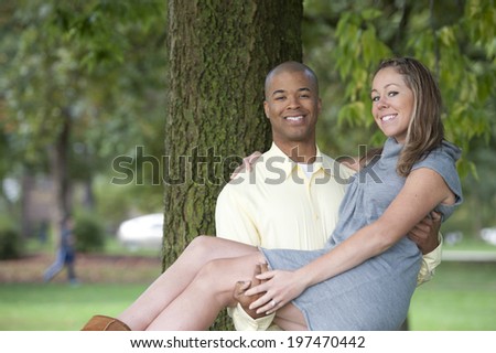 A beautiful, happy and young interracial couple posing next to a tree on a sunny day.