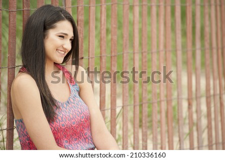 A young and happy brunette female model looking to the right side at the beach on a sunny day wearing a beautiful dress.