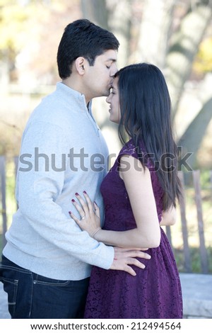A young and happy Indian man kissing his fiance on the forehead on a sunny day in the Fall.