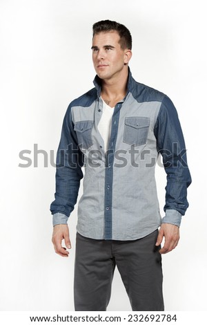 Attractive white caucasian male model wearing a jean shirt and gray pants posing in a studio on a white background while looking away from the camera.
