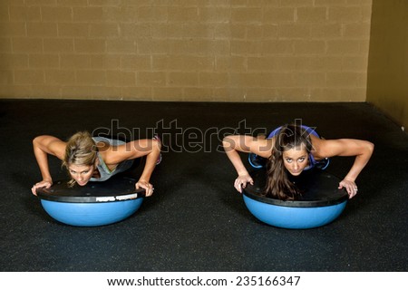 Two athletic trainers doing a push up on a bosu ball in a gym.
