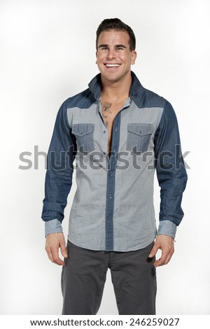 Attractive white caucasian male model laughing while wearing a jean shirt and gray pants posing in a studio on a white background while looking at the camera.