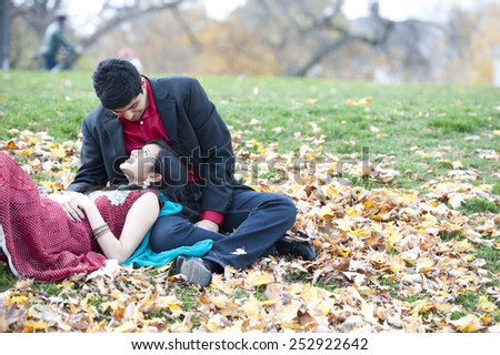 A young and happy Indian couple posing on a pile of leaves in the fall on a cloudy day.
