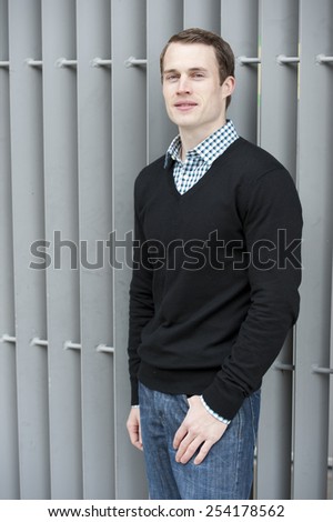 A young white male model posing on a gray background on a sunny day.