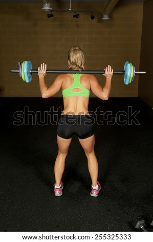 The back a young brunette doing a squat with a barbell in a gym.
