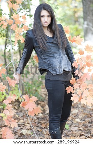 A young girl posing in a leather jacket and black outfit in a forest during the fall on a sunny day.