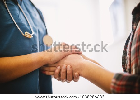 Close up portrait view of middle aged professional nurse holding hands with a patient.