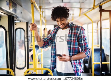 Young cheerful handsome man is enjoying the music during his ride and holding onto the bar while standing in a bus.