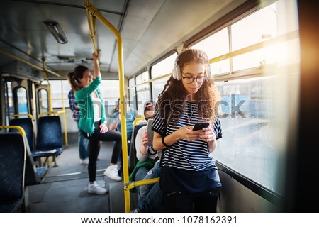 Young beautiful girl is leaning against the bars on a bus and listening to music on headphones.