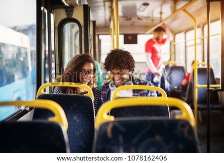 Young happy gorgeous couple is sitting together in a bus and smiling while looking at something hidden behind the bus seat.