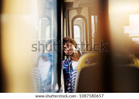 A young handsome bored man is sitting in a bus seat leaned and looking through the window as he waits for arrival to his destination.