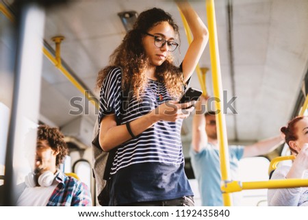 Curly young student girl holding for a bar in a public transportation and listening to the music over her telephone.