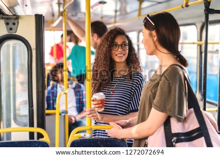 Two girls standing in a bus chatting and drinking coffee.