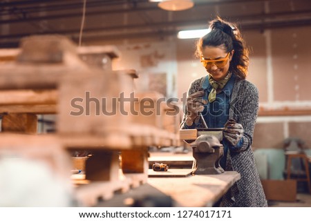 Girl in carpentry workshop doing wood job with protective glasses on.