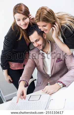 Business, technology, teamwork and people concept - smiling business team with laptop computers having discussion over office background.