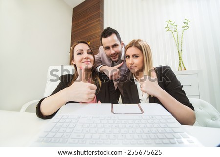 Thumbs up office workers looking at laptop screen. Different angle.