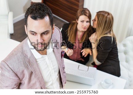 Gossip girls at office, handsome businessman portrait and gossip girls out of focus in background.